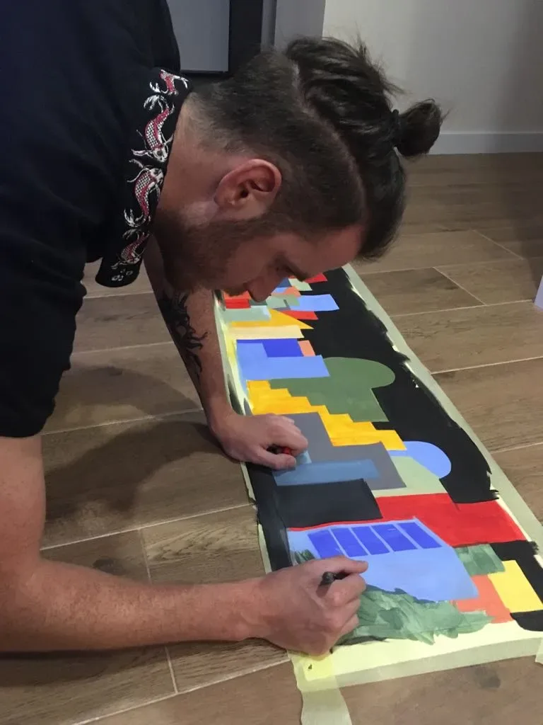Nico Belico hand-painting a long geometric artwork on the studio floor